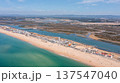 Aerial view shows Praia de Faro with people on the beach and Ria Formosa nearby. The coastline stretches as boats are visible in the water on a clear day 137547040