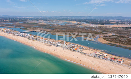 Aerial view shows Praia de Faro with people on the beach and Ria Formosa nearby. The coastline stretches as boats are visible in the water on a clear day 137547040