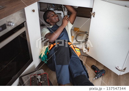 Plumber fixing pipes under kitchen sink Plumber fixing pipes under kitchen sink 137547344
