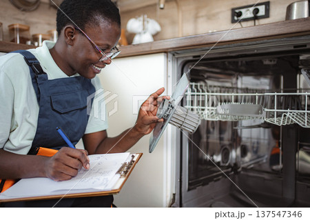 Technician inspecting dishwasher filter and taking notes on clipboard Technician inspecting dishwasher filter and taking notes on clipboard 137547346