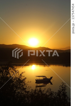 Small fishing boat with reflection in calm sea at sunrise. Small fishing boat with reflection in calm sea at sunrise. 137547454