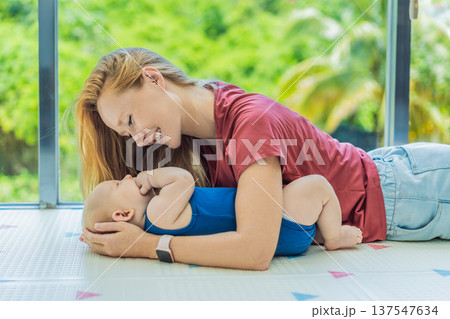 Mother and baby lying on a soft play mat at home, playing, talking and sharing a joyful moment together. Authentic family lifestyle, early childhood development and emotional bonding. Parenting and 137547634