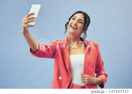 Phone, selfie and woman with a smile from social media and profile picture for creative job in studio. Influencer, happy and female person with makeup and fashion with blue background and model Phone, selfie and woman with a smile from social media and profile picture for creative job in studio. Influencer, happy and female person with makeup and fashion with blue background and model 137547727