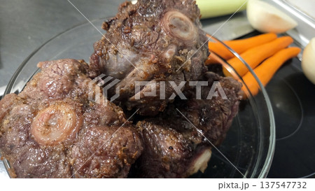 Delicious oxtail dish preparation with fresh carrots in a kitchen setting. Traditional Spanish dish. Typical food of Spain Delicious oxtail dish preparation with fresh carrots in a kitchen setting. Traditional Spanish dish. Typical food of Spain 137547732