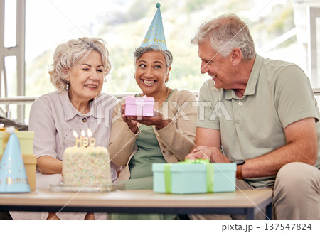 Birthday, senior friends with cake and gift for celebration in living room, smile and candles in retirement. Happiness, old people and party with dessert, surprise and elderly man with women on sofa. Birthday, senior friends with cake and gift for celebration in living room, smile and candles in retirement. Happiness, old people and party with dessert, surprise and elderly man with women on sofa. 137547824