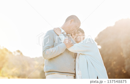 Nature, sunset and senior couple hugging, laughing and bonding on a romantic date in a park. Happy, smile and elderly woman and man in retirement embracing with love, care and happiness in a field. 137548875