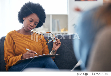 Therapist on sofa, writing notes with patient, advice and help in psychology, listening and mental health care. Conversation, support and black woman on couch with client, psychologist in counseling. Therapist on sofa, writing notes with patient, advice and help in psychology, listening and mental health care. Conversation, support and black woman on couch with client, psychologist in counseling. 137549040