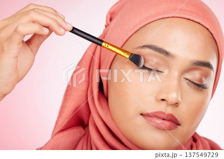 Makeup, brush and muslim woman in studio with eyeshadow, application and wellness on pink background. Beauty, glamour and female model with hijab, cosmetics and luxury, makeover or transformation Makeup, brush and muslim woman in studio with eyeshadow, application and wellness on pink background. Beauty, glamour and female model with hijab, cosmetics and luxury, makeover or transformation 137549729