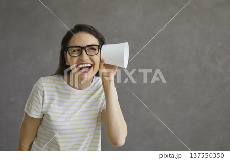 Young funny and curious woman on a gray background overhears a conversation with a plastic cup. 137550350