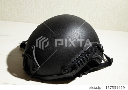 A matte black tactical helmet with integrated side rails for mounting accessories and a secure chin strap is displayed on a light-colored surface 137551429