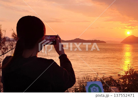 夕日をスマホ撮影する女性の後ろ姿 夕日をスマホ撮影する女性の後ろ姿 137552471