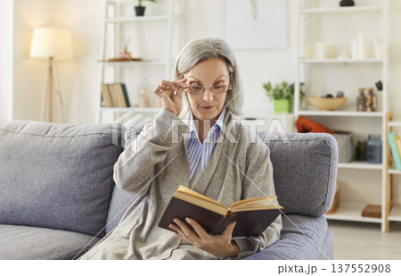 Retired old senior woman, pleasant elderly person alone at home, reading a book wearing glasses Retired old senior woman, pleasant elderly person alone at home, reading a book wearing glasses 137552908