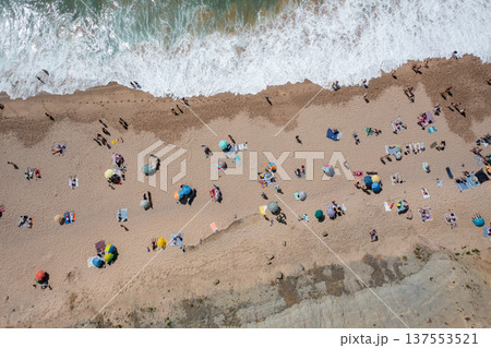Tourists and colorful parasols on sandy seashore 137553521