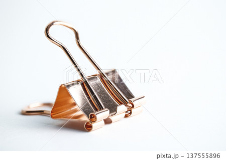 A single metallic copper-colored paper clamp standing upright on a white surface in soft light A single metallic copper-colored paper clamp standing upright on a white surface in soft light 137555896