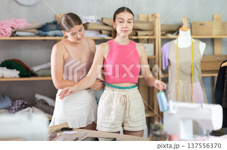 Young seamstress takes body measurements from adult woman 137556370