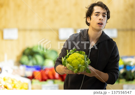Young man chooses broccoli at vegetable shop Young man chooses broccoli at vegetable shop 137556547
