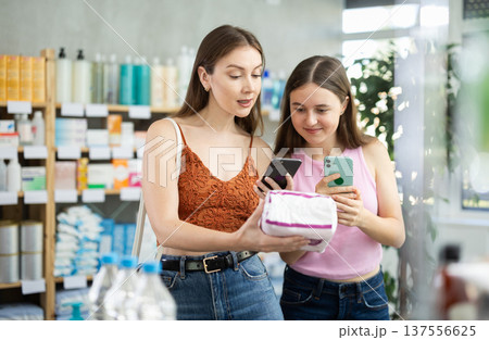 Mom and daughter scan a package with pads on their phone at a pharmacy 137556625