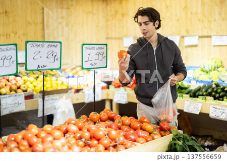 Young man chooses tomatoes in store Young man chooses tomatoes in store 137556659