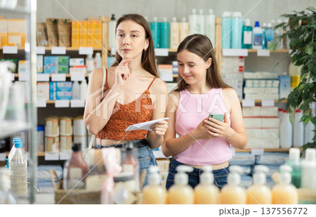Daughter and mother read a prescription and look for medicine in modern pharmacy 137556772