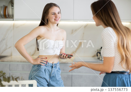 Two young women talking while standing in kitchen 137556773