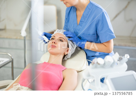 Young girl getting facial rf-lifting procedure of smoothes wrinkles and tightens skin on face in beauty salon. Concept of professional cosmetology 137556785