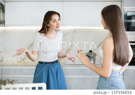 Two young women talking while standing in kitchen Two young women talking while standing in kitchen 137556858