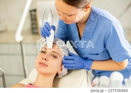 Caucasian brunette young girl lying in spa while having facial treatment procedures with modern technologies vibrating shovel leather knife. Soften skin keratin, deep clear skin dirt. Hardware 137556868