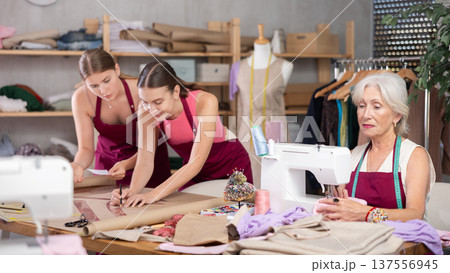 Elderly seamstress working alongside fashion designers in an atelier Elderly seamstress working alongside fashion designers in an atelier 137556945