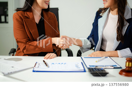 Woman lawyer hand and women client shaking hand collaborate on working agreements with contract documents Woman lawyer hand and women client shaking hand collaborate on working agreements with contract documents 137556980
