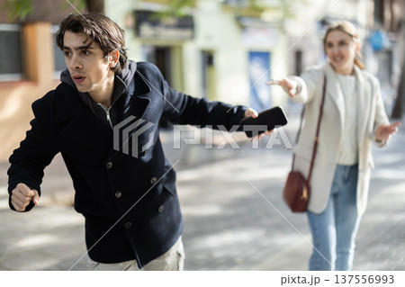 Male thief trying to snatch mobile phone of frightened woman on city 137556993