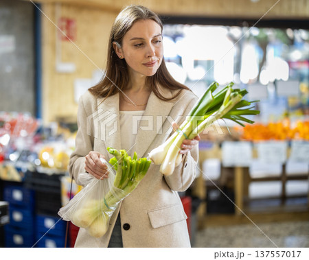 Girl near vegetable stand in store choose pick up leek Girl near vegetable stand in store choose pick up leek 137557017