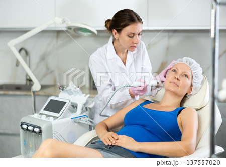 Adult woman getting oxygen face therapy in beauty salon. Professional skin care treatment, atomized nutrients to Supplement, skin nutrition. Innovative technique Adult woman getting oxygen face therapy in beauty salon. Professional skin care treatment, atomized nutrients to Supplement, skin nutrition. Innovative technique 137557020