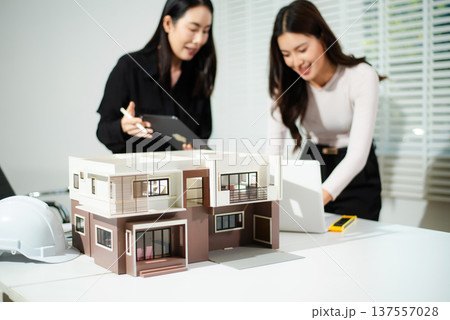 Architects reviewing house model and digital plans on tablet and laptop, concept of modern architecture, real estate development, housing design Architects reviewing house model and digital plans on tablet and laptop, concept of modern architecture, real estate development, housing design 137557028