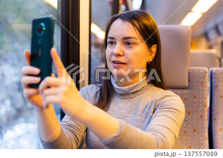 Woman taking photos with smartphone through window glass while travelling by train Woman taking photos with smartphone through window glass while travelling by train 137557089