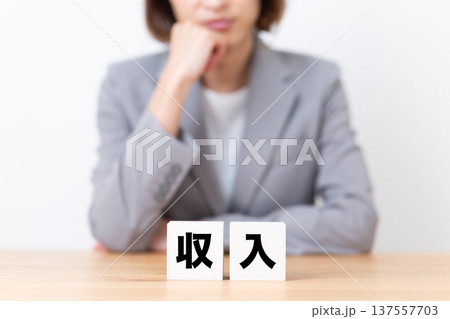 収入のブロックと悩むスーツ姿のミドル女性 収入のブロックと悩むスーツ姿のミドル女性 137557703