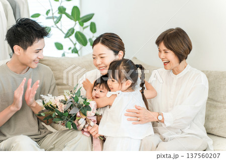 ママに母の日,誕生日に花束をプレゼントする娘とリビングに集まる三世代家族 ママに母の日,誕生日に花束をプレゼントする娘とリビングに集まる三世代家族 137560207