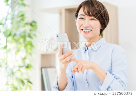 リビングでスマホを操作するミドル女性。 リビングでスマホを操作するミドル女性。 137560372