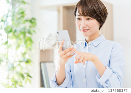 リビングでスマホを操作するミドル女性。 137560375
