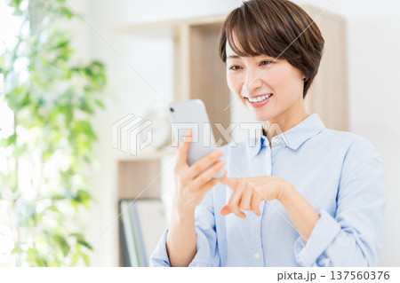 リビングでスマホを操作するミドル女性。 137560376