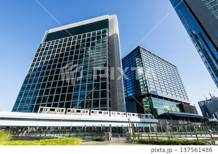 Low-angle view of a New Transit Yurikamome line train running on the elevated track with modern skyscrapers in Shiodome, Minato, Tokyo, Japan. It's an automated guideway transit service in Tokyo. 137561486