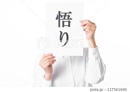 悟りと書かれた紙を両手で持つ白いシャツを着た人物 137561690