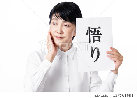 悟りと書かれた紙を持ち頬に手をあて物思いにふけるシニア女性 悟りと書かれた紙を持ち頬に手をあて物思いにふけるシニア女性 137561691