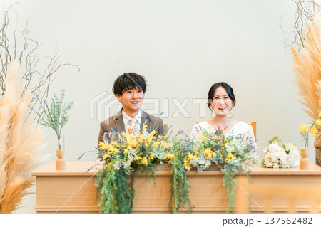 結婚式の披露宴の高砂席で挨拶を聞く新郎新婦 結婚式の披露宴の高砂席で挨拶を聞く新郎新婦 137562482