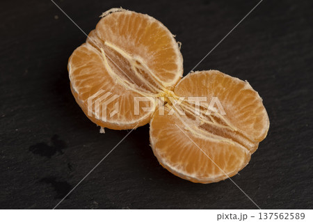 sliced peeled orange tangerine on a black slate table, ripe orange small mandarin without peel on a black slate board, tangerine divided into small slices 137562589