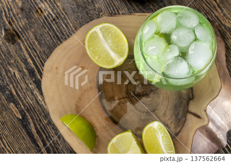 cold green lime-flavored carbonated drink with lots of gas bubbles and whole pieces of fresh sour lime, sweet green-colored drink poured into a glass with ice 137562664
