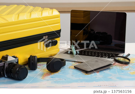 Travel Essentials. Yellow suitcase, laptop, and camera on world map. Travel Essentials. Yellow suitcase, laptop, and camera on world map. 137563156