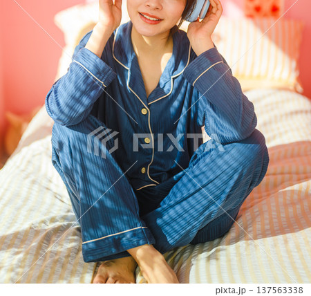 パジャマ姿の女性がベッドで音楽鑑賞 ：はっぴぃぽっぷ 137563338