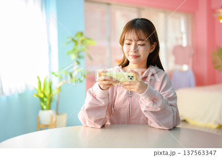 部屋でスマホゲームをする若い女性 ：はっぴぃぽっぷ 137563347