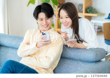 リビングでスマホを見る若いカップル	 137564040