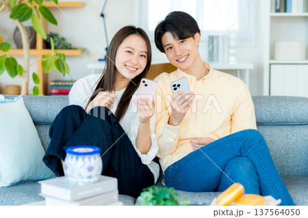 リビングでスマホを見る若いカップル	 137564050
